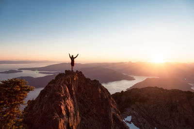 Silhouette person standing on rock against sky during sunset