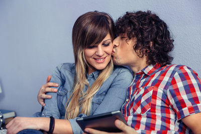 Close-up of man kissing girlfriend while using digital tablet at home