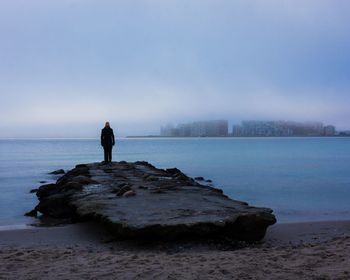 Man standing on rock at beach against sky