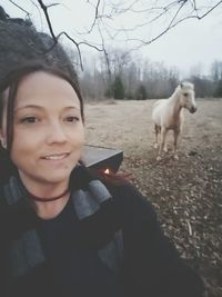 Portrait of young woman holding dog against sky