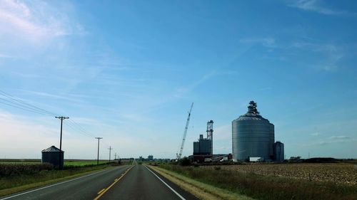 Road amidst field against blue sky