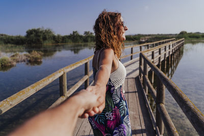 Woman sitting on railing by lake against sky