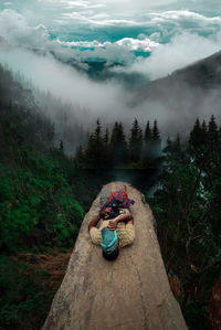 Woman sitting on land by trees against sky