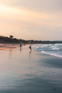 People on beach against sky during sunset