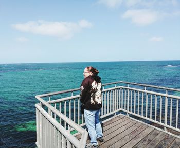 Rear view of young woman standing by railing against sea