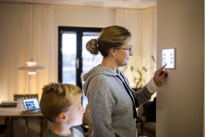 Son looking at mother using digital tablet mounted on wall at smart home