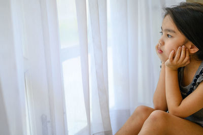 Portrait of woman looking away while sitting on window at home