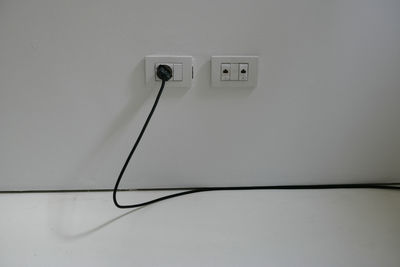 Close-up of plug with cable on white wall