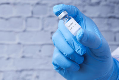 Close-up of hand holding vial against wall