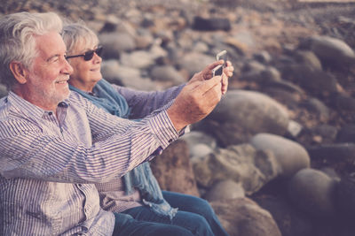 Couple taking selfie from mobile phones on rocks at beach