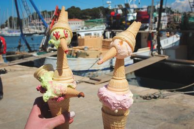 Close-up of hand holding ice cream cones at harbor