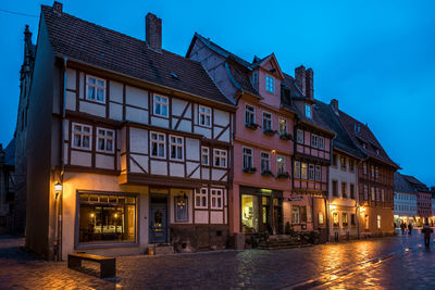 Illuminated building by street against sky at dusk