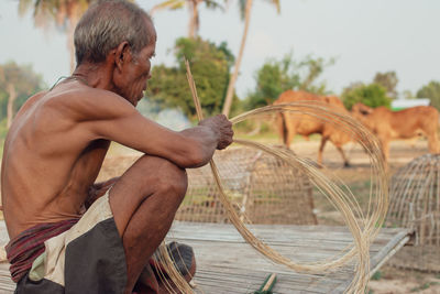 Shirtless senior man making straw basket