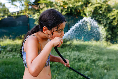 Child drinking directly from hosepipe on a sunny hot day in the garden