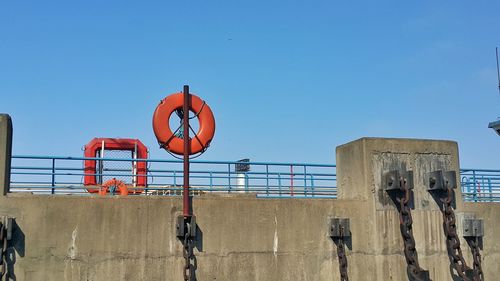 Life belt hanging on pole at harbor against clear blue sky