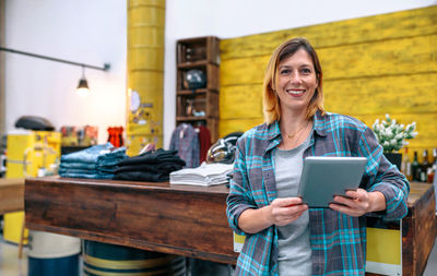 Portrait of young woman using digital tablet while standing in cafe