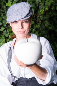 Portrait of woman wearing cap holding while apple at backyard