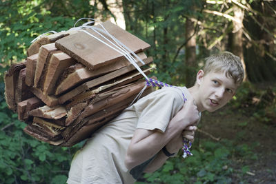 Teenage boy carrying firewood in forest