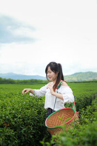 Smiling woman with basket picking leaves in tea plantation field