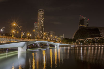 Illuminated bridge over river against buildings in city at night