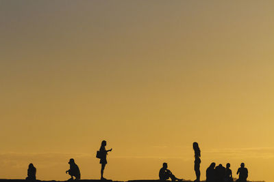 Silhouette people standing on beach against clear sky during sunset