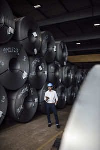 Male entrepreneur using digital tablet while standing by steel rolls at industry