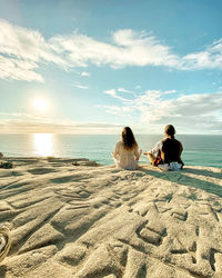 People sitting on beach by sea against sky
