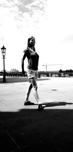 Full length of woman skateboarding on street against sky