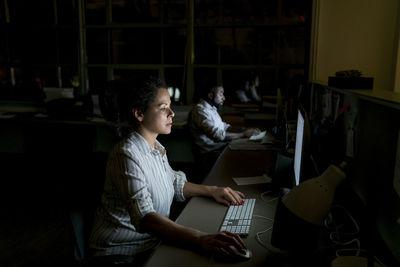 Colleagues working on desktop computers at desk in dark office