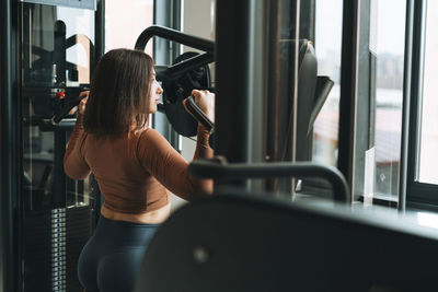 Young fitness brunette woman training for back muscles equipment at gym