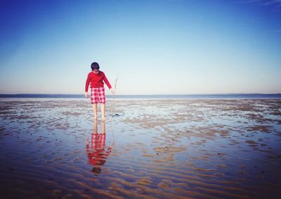 Boy walking at beach against clear blue sky