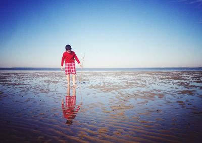 Boy walking at beach against clear blue sky