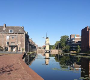 Canal amidst buildings in town against clear blue sky