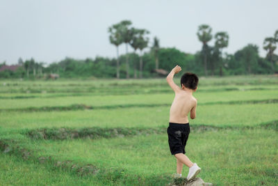 Rear view of shirtless boy standing on field