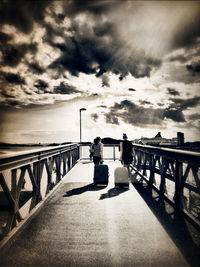 People walking on bridge against cloudy sky