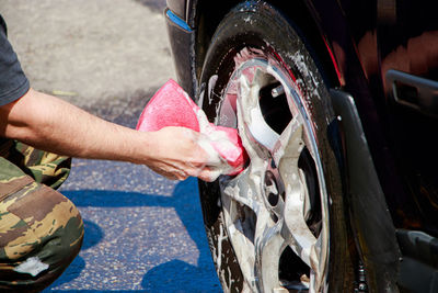 Man washes car wheel. male hand holds pink sponge with soapy foam for cleaning. car wash 