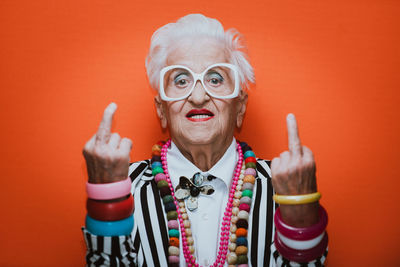 Portrait of stylish senior woman wearing colorful jewelry showing middle finger against red background