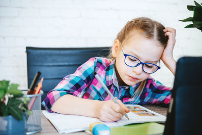 Little girl in eyeglasses studying online at home, a primary school girl with computer having zoom