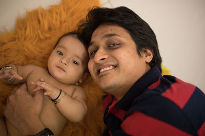 High angle portrait of smiling father with cute daughter lying on bed at home