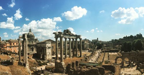 Coliseum by buildings against cloudy sky