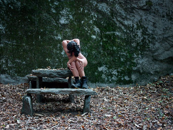 Full length of shirtless man sitting in forest