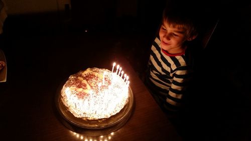 High angle view of smiling boy looking at illuminated birthday cake in darkroom at home