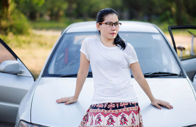 Confident young woman leaning on car parked at field