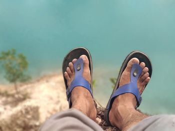 Low section of man wearing sandals sitting over sea