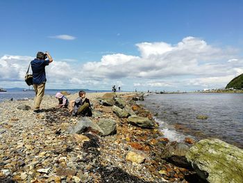 People on rocks at beach against sky