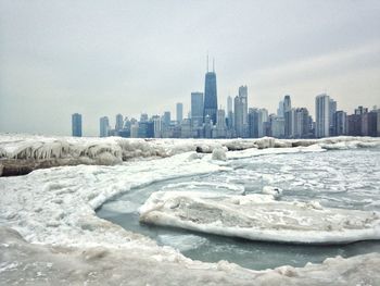 Sea by buildings against sky in city during winter