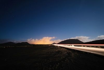 Road by mountains against blue sky at night