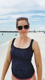 Portrait of young woman wearing sunglasses standing at beach against sky