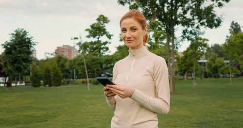 Woman using mobile phone while doing sports in the park. 