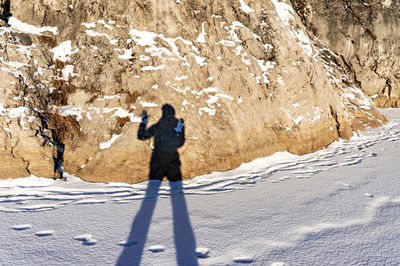 Female shadow with long legs and raised hand on fresh snow and rock on winter day. light and shadow